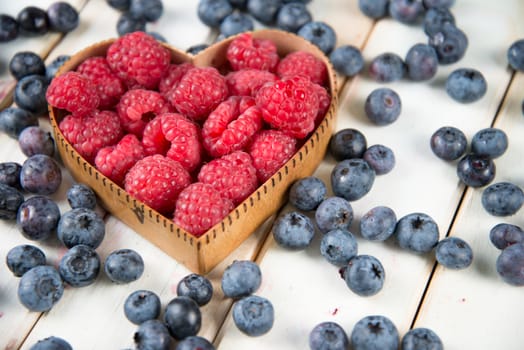 fresh organic raspberries and blueberries in heart style shape basket  on white background retro kitchen table