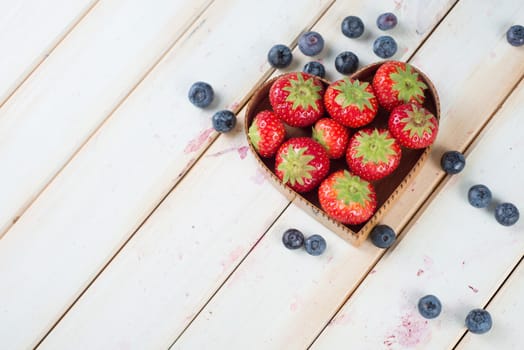 fresh organic strawberries and blueberries in heart style shape basket  on white background retro kitchen table