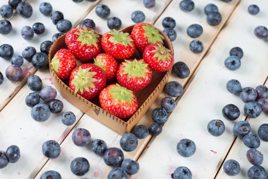 fresh organic strawberries and blueberries in heart style shape basket  on white background retro kitchen table