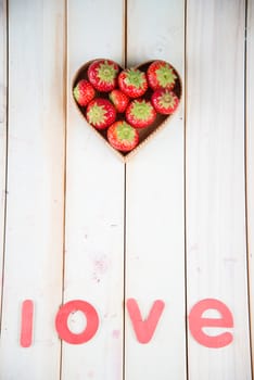 fresh organic strawberries in heart style shape basket  on white background retro kitchen table and love letters