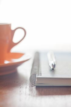 Orange coffee cup, pen and notebook on wooden table, stock photo