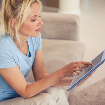 Side view of a young woman using digital tablet in the living room at home