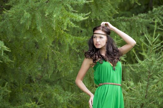 Beautiful young woman in green dress, against green of summer park