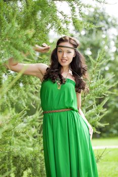 Beautiful young woman in green dress, against green of summer park