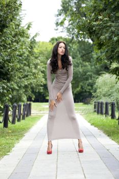 Full growth, beautiful young woman in sexy long gray dress, walking in summer park