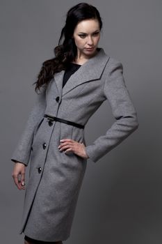 Beautiful young woman in autumn coat against gray background
