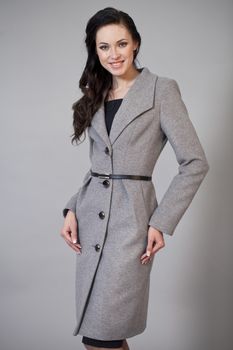 Beautiful young woman in autumn coat against gray background
