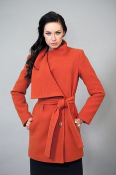 Beautiful young woman in a bright orange coat against gray background
