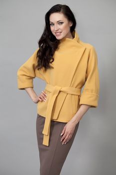 Beautiful young woman in yellow coat against gray background