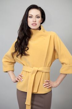 Beautiful young woman in yellow coat against gray background