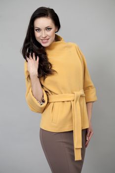 Beautiful young woman in yellow coat against gray background