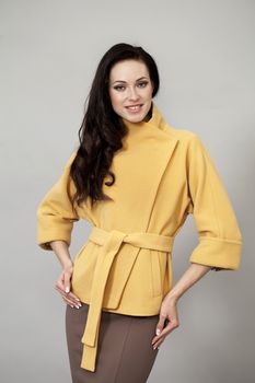 Beautiful young woman in yellow coat against gray background