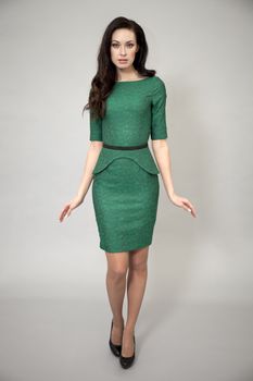 Young beautiful caucasian brunette in green dress posing on grey background