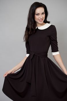 Young beautiful caucasian brunette in fashion dress posing on grey background