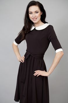 Young beautiful caucasian brunette in fashion dress posing on grey background