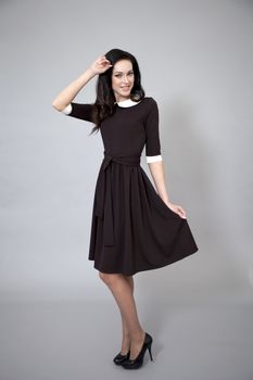 Young beautiful caucasian brunette in fashion dress posing on grey background