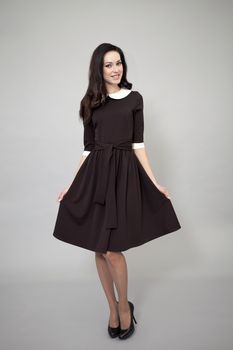 Young beautiful caucasian brunette in fashion dress posing on grey background