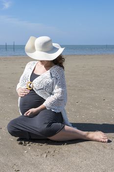 adult pregnant woman holding her hands on her belly on the beach with sand and sea