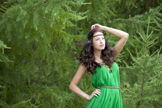 Beautiful young woman in green dress, against green of summer park