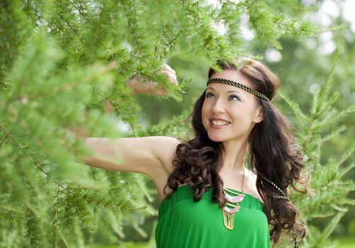 Beautiful young woman in green dress, against green of summer park