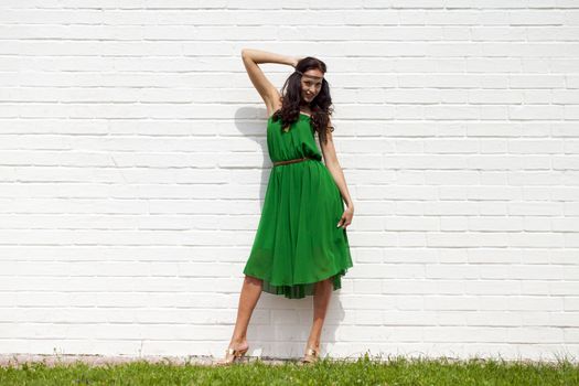 Beautiful young woman in green dress, against white wall