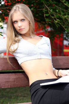 Portrait of blonde young woman sitting on the bench in summer park