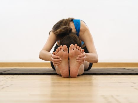 Photo of a woman in her twenties grabbing her feet and stretching her leg muscles. Focus is on the feet and hands.
