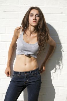 Beautiful sexy young brunette in blue jeans on white brick wall