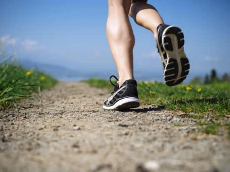Photo of the legs and shoes of a young woman jogging on a gravel path down a country path. Slight motion blur visible.