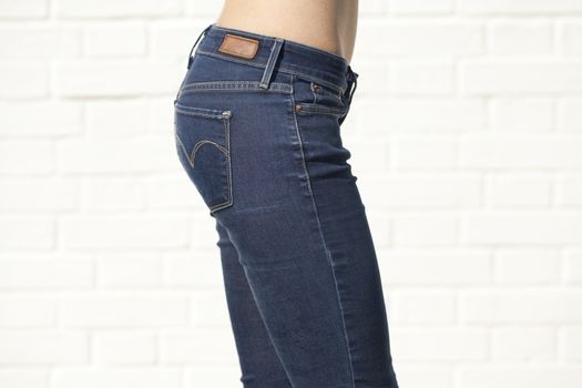 Woman in blue jeans with naked back isolated on white brick wall
