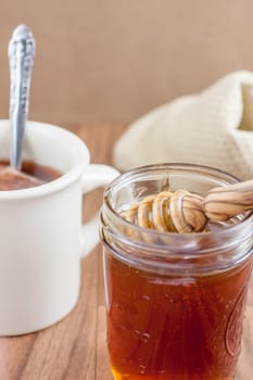 A jar of raw natural honey in a canning jar with a wooden dipper on a wooden table.