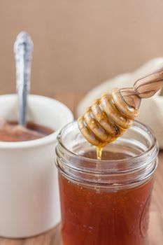 A jar of raw natural honey in a canning jar with a wooden dipper on a wooden table.