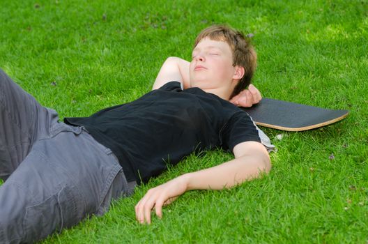 Teenager with skate resting or sleeps on the grass after active skateboarding