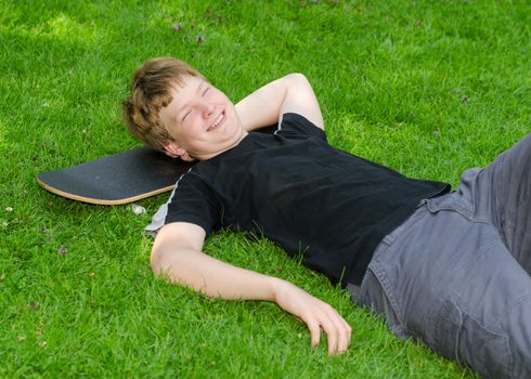 Laughing guy relax on skateboard in park grass and rest after an active leisure