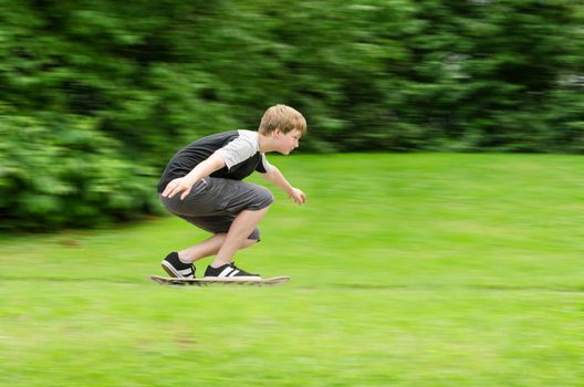 Young teen guy fast rides a skateboard in park. Slow shutter photo in action with blurred trees and grass background and copy-space place.