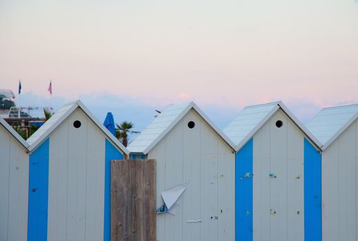 Blue and white wooden beach huts, under sunset lights