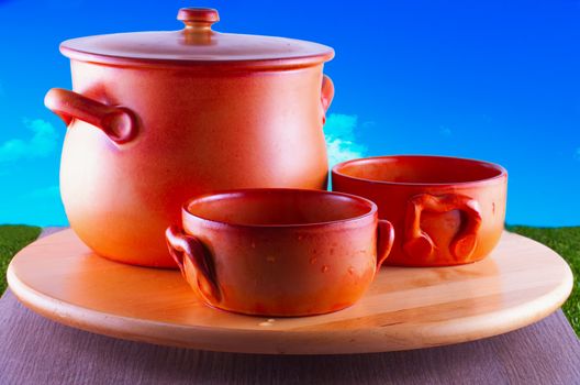 Crock pots over round wooden plate, blue sky on the back