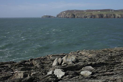 A view from rocks across a bay to south stack lighthouse in the distance, Wales coast path, Anglesey, Wales, uk.