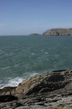 A view from rocks across a bay to south stack lighthouse in the distance, Wales coast path, Anglesey, Wales, uk.