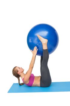 Side view of a fit young woman exercising with fitness ball over white background