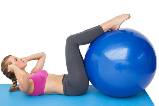Side view of a fit young woman exercising with fitness ball over white background