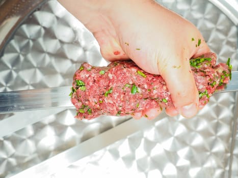 A chef making shish kebab of red meat with parsley over metal plate