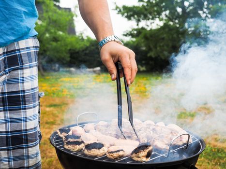 Male person with food tweezers barbequing with lot's of smoke