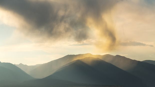 Rain with falling rain spout over the mountains of Colorado with the sun illuminating the falling raindrops on the summit