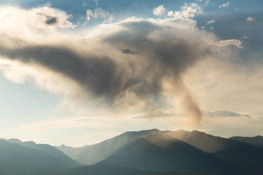 Rain with falling rain spout over the mountains of Colorado with the sun illuminating the falling raindrops on the summit