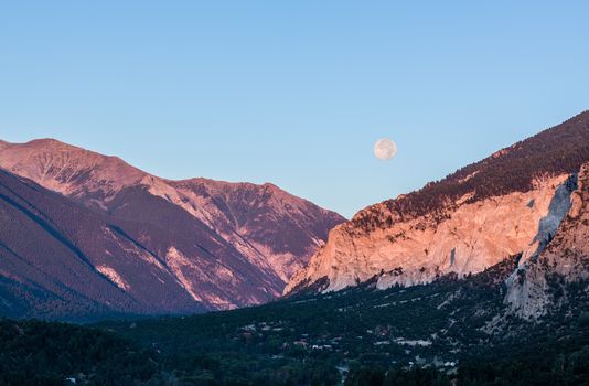 Valley by chalk white cliffs of Mount Princeton near Buena Vista in Colorado as setting moon drops over horizon at sunrise