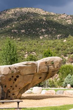 Climbing wall with hand holds and bolted fasteners with real mountain and rocks in the background