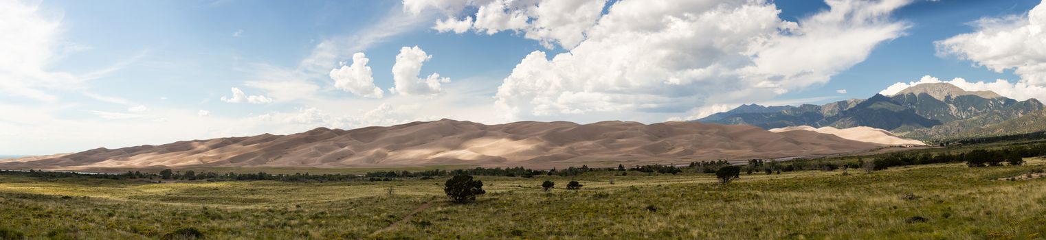 Wide high resolution stitched panorama of the dunes at Great Sand Dunes National Park in Colorado with the mountains behind. Unusual to see clouds over the sand