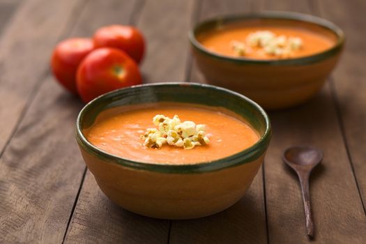 Ecuadorian tomato and potato cream soup served with popcorn on top in rustic bowls (Selective Focus, Focus on the front of the popcorn on the soup)