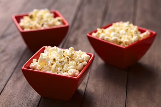 Three red bowls of freshly prepared salted popcorn (Selective Focus, Focus one third into the popcorn in the first bowl)